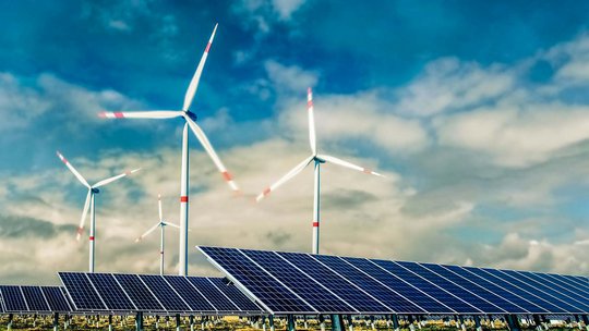 Windräder vor blauem Himmel mit Wolken, dazu Solaranlagen