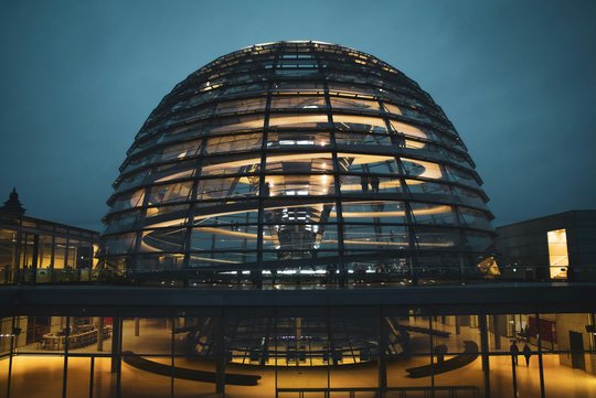 Die Kuppel des Reichstagsgebäudes hell erleuchtet bei Nacht in einer Seitenansicht. 