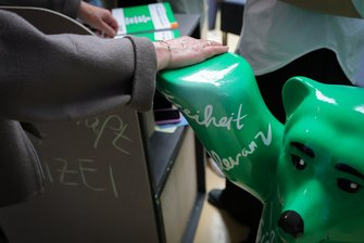 Eine Hand liegt auf der Hand eines grünen Kunstoffbären. 