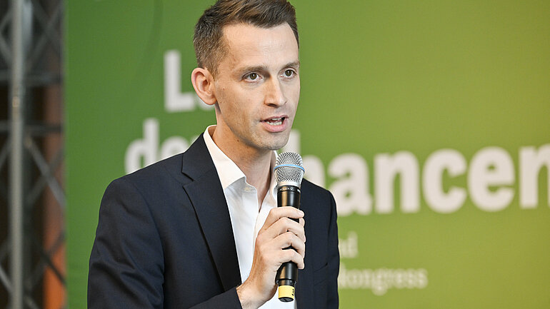 Andreas Audretsch steht vor einem grünen Hintergrund und spricht in ein Mikrofon. 