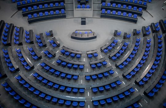 Ein Blick von oben in den leeren Plenarsaal im Reichstagsgebäude in Berlin. Viele blaue Sitze sind zu sehen.