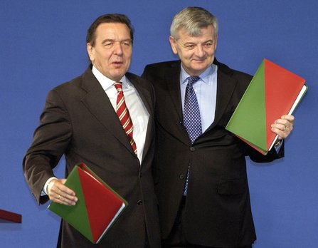 Gerhard Schröder und Joschka Fischer stehen nebeneinander, beide halten den rot-grünen Koalitionsvertrag in der Hand