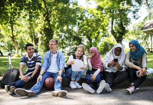 Eine diverse Gruppe Jugendlicher sitzt nebeneinander in einem Park. 