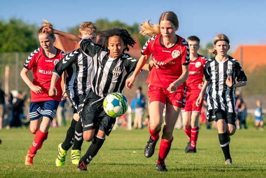 Jugendliche beim Fußballspielen: Eine Mannschaft in Rot, eine andere in schwarz-weißen Trikots kämpfen um den Ballbesitz und laufen auf die Kamera zu.