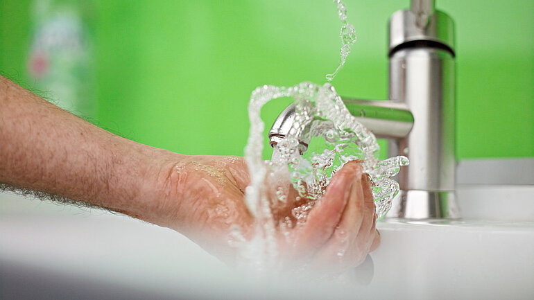 Wasser sprudelt aus einem Hahn in eine geöffnete Hand.