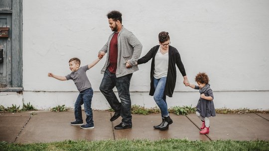 Kind, Vater, Mutter, Kind Hand in Hand in einer Reiher vor einer weißen Wand.