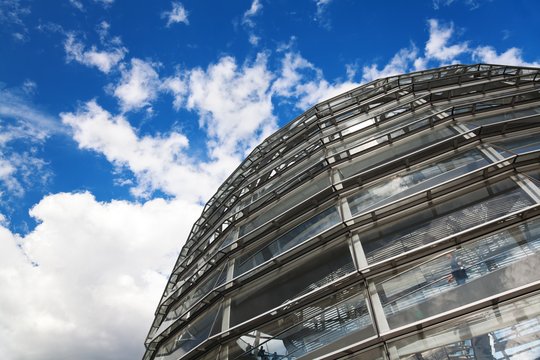 Ein Foto der Kuppel des Reichstagsgebäudes, leicht angeschnitten und vor blauem Himmel mit weißen Wolken