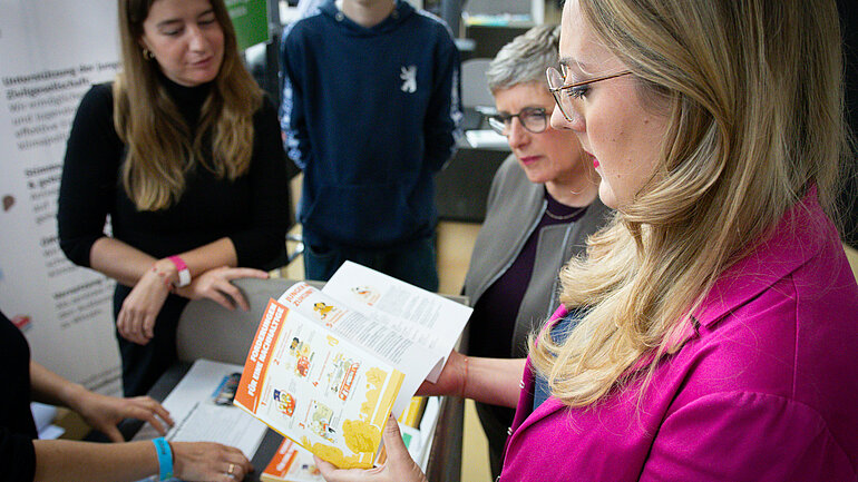 Katharina Dröge und Britta Haßelmann stehen nebeneinander und schauen sich eine Publikation an