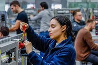 Eine Frau bei der Arbeit: Sie steht in einer Fertigungshalle an einer Maschine.