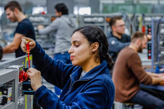 Eine Frau bei der Arbeit: Sie steht in einer Fertigungshalle an einer Maschine.