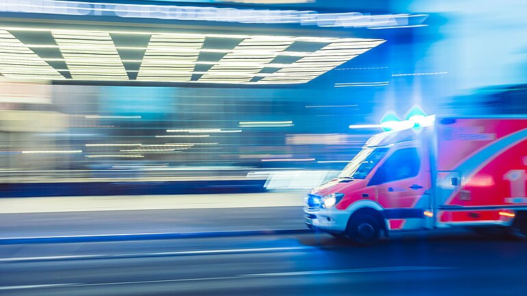 Ein Rettungswagen fährt mit Blaulicht auf einer Straße. 