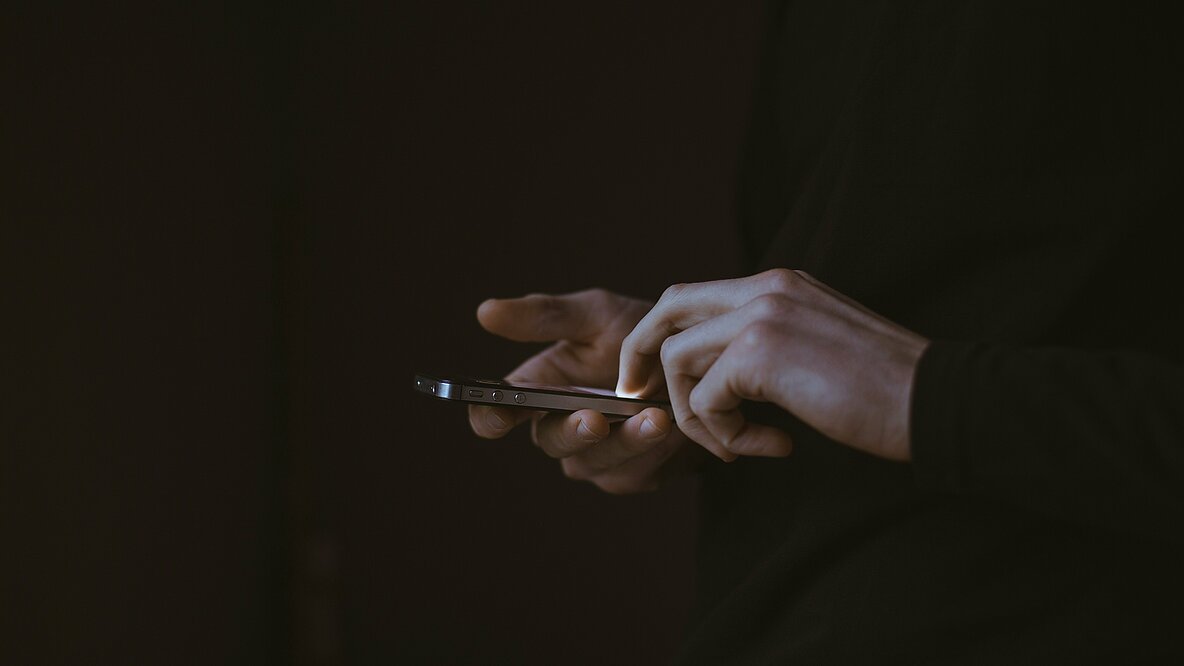 Zwei Hände halten ein Smartphone, der Hintergrund ist schwarz. 