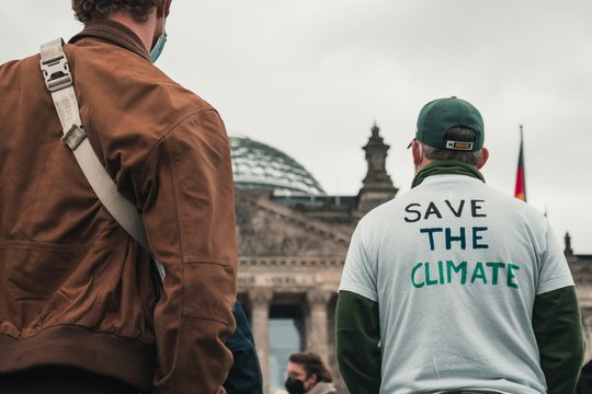 Zwei Demonstrierende stehen vor dem Reichstagsgebäude, sie stehen mit dem Rücken zur Kamera, eine der Personen trägt ein T-Shirt mit der Aufschrift "Save the climate".