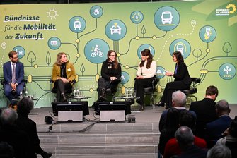 5 Personen sitzen nebeneinander auf der Bühne.