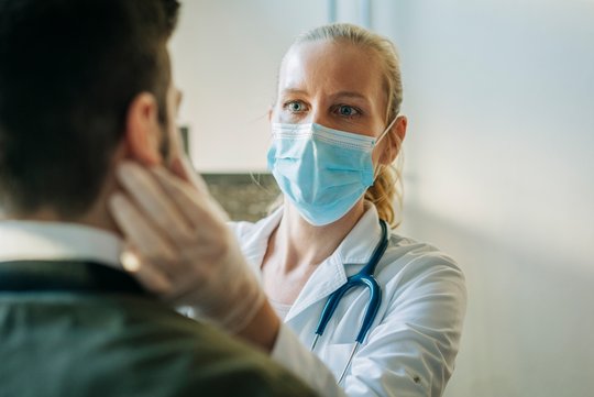 Eine Ärztin mit einer Maske untersucht einen Patienten am Kopf.