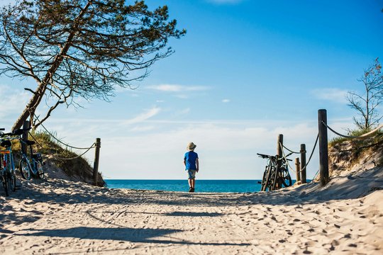 Ein Junge spaziert auf das Meer zu, er geht einen Strandaufgang an der Ostsee entlang.